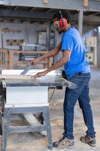 Fototapeta Table saw cutting long wood board in carpentry workshop, with dust collection hose attached