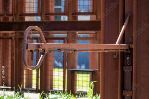 Close-up view of a rusty industrial valve handle attached to a metal construction. Detailed texture and warm tones with shallow depth of field in an industrial environment.