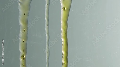 Macro vertical view of thick yellow-green oily liquid droplets streaming down a smooth transparent glass surface.