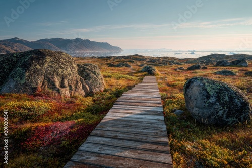 Wooden Boardwalk Path Through Autumn Tundra Landscape Towards Distant Mountains and Ocean.