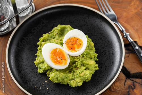 Mashed avocado and boiled eggs on black plate, healthy keto meal