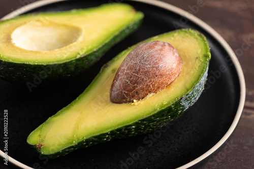 Avocado cut in halves on a plate, wooden background. Healthy tropical exotic fruit rich in Omega 3 fatty acids