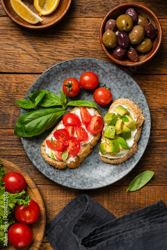 Italian bruschetta with cream cheese, tomatoes, avocado chunks and olives. Table top view