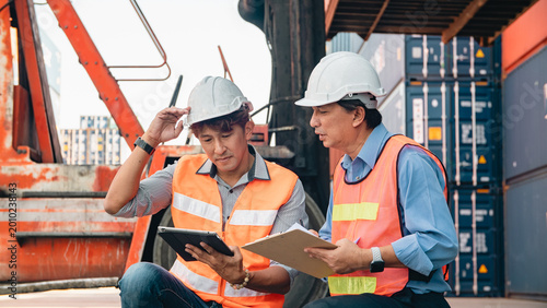 Obraz na plátně Asian worker logistics engineer safety vest hard hat container teamwork tablet c