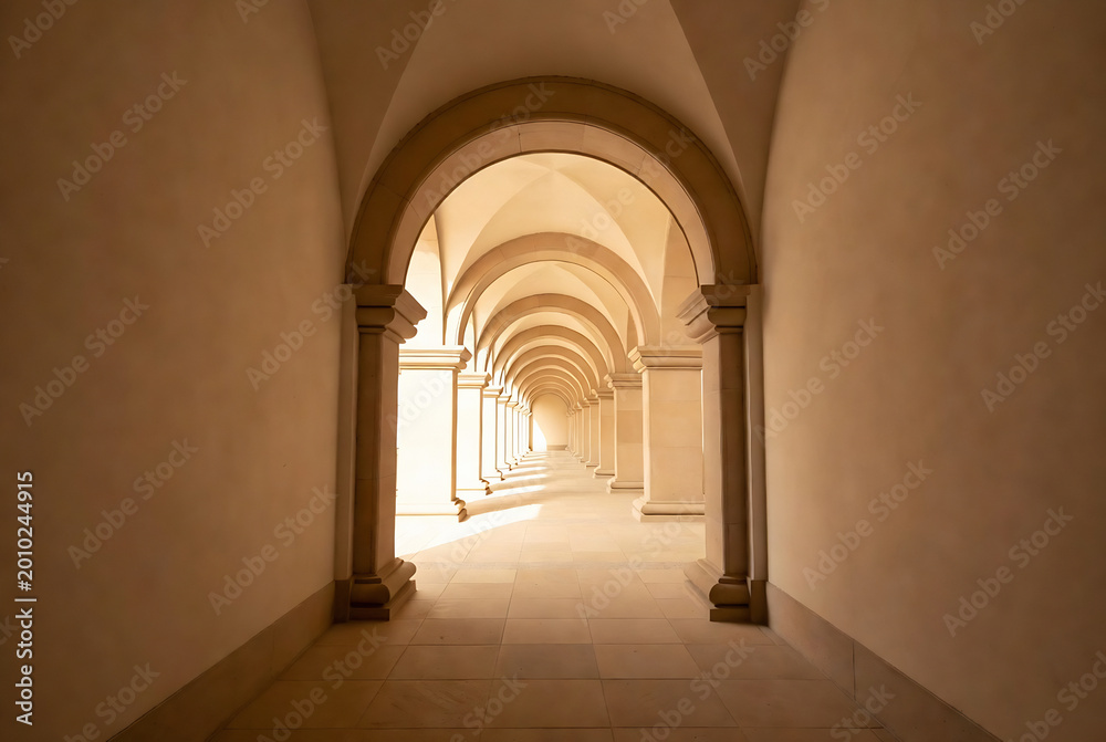 Fototapeta premium A long, arched corridor with columns leads into a distant light.