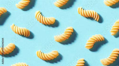 raw fusilli pasta scattered on blue background. Top view of uncooked spiral noodle pattern. Healthy food ingredient for Italian cuisine cooking. Minimal culinary textured wallpaper