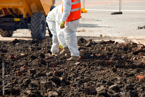 Εκτύπωση καμβά Two workers in protective gear remove asbestos from contaminated ground filled w