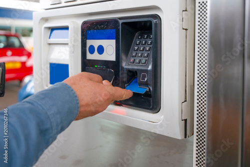Slika na platnu Man pays for fuel at a gas station using a credit card during daylight hours in