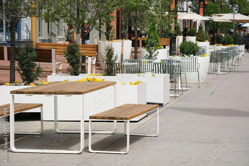 Vászonkép Outdoor cafe with white planters, wooden benches and metal tables lining a sunlit urban pedestrian plaza and wide sidewalk, contemporary terrace seating