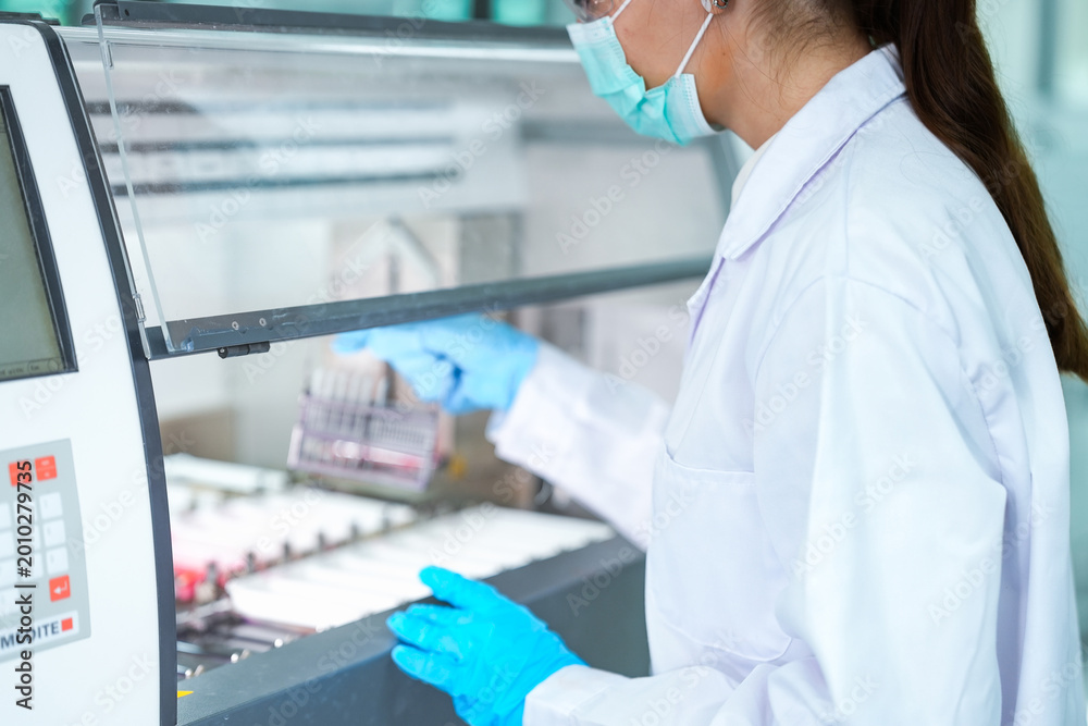 Fototapeta premium Medical scientist loading slide rack into automated stainer machine. Lab technician in protective gear processing histology samples in sterile hospital laboratory.