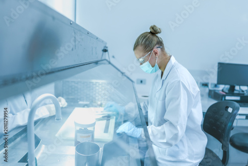 Billede på lærred Lab technician working behind glass sash of fume hood for safety