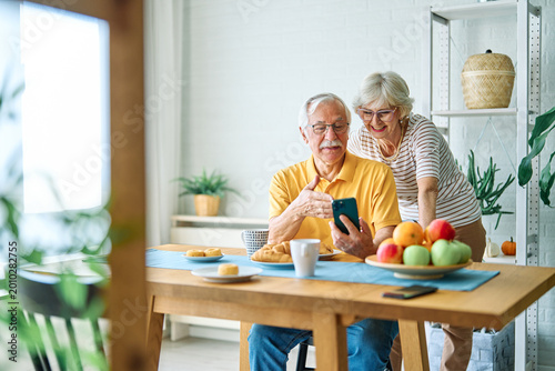 Fotografie Portrait of an elderly senior couple having breakfast and using a smart phone at home