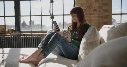 Woman enjoying her Smartphone in sunlight on Sofa using Banking app