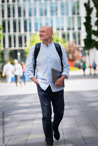 Smiling middle-aged man wearing backpack and holding notebook in his hand outdoors