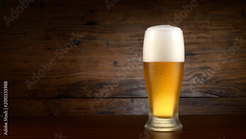 Ice-cold pilsner beer in a glass with foam and a wooden bottom.