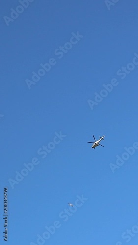 Helicopter flying in a clear blue sky above fluffy clouds during afternoon hours. High quality FullHD footage