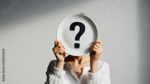 Person holding plate with question mark, obscuring face and representing concepts of identity, doubt, and finding solutions