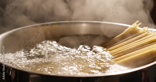 Cooking spaghetti in boiling water with steam rising, showcasing a kitchen setting