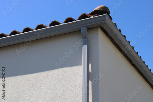 Gouttière rectangulaire avec descente en aluminium de forme rectangulaire couleur grise, installée sur la façade d’une maison.