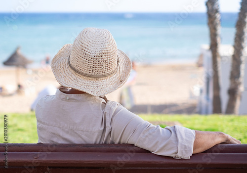 фотографія Woman in Straw Hat Sitting on Bench Overlooking Beach and Sea Enjoying Summer Re
