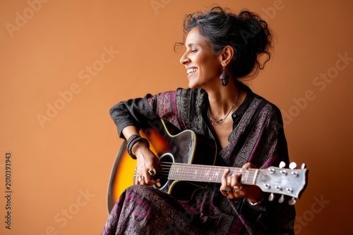 Portrait of a smiling indian woman in her 40s playing the guitar isolated on soft orange background