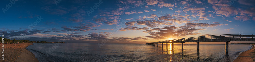 Obraz premium The pier in Boltenhagen on the Baltic Sea bathed in the warm light of sunrise.