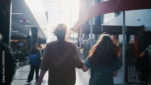 Young couple holding hands and running through a busy airport terminal to catch their flight