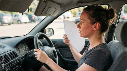 A female driver uses a paper for hand fanning face in summer heat inside a warm car, a picture for auto air conditioning articles.