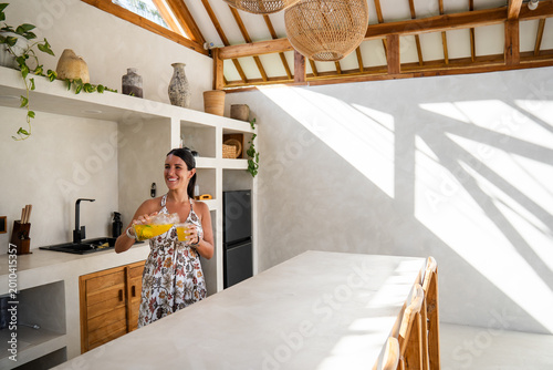 Woman smiling while pouring a refreshing drink in a bright minimalist villa kitchen