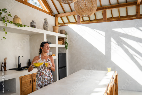 Woman enjoying a healthy beverage in a modern tropical villa kitchen with natural light