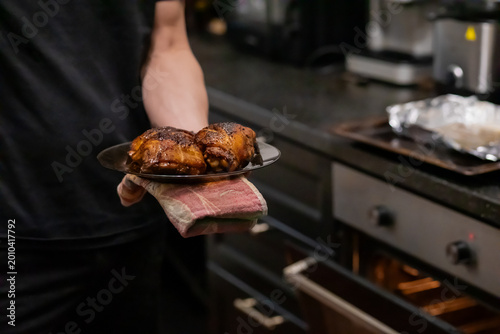 Slika na platnu Man holding black plate with roasted chicken thighs