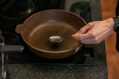 Foto Man pouring oil into heated frying pan on electric stove