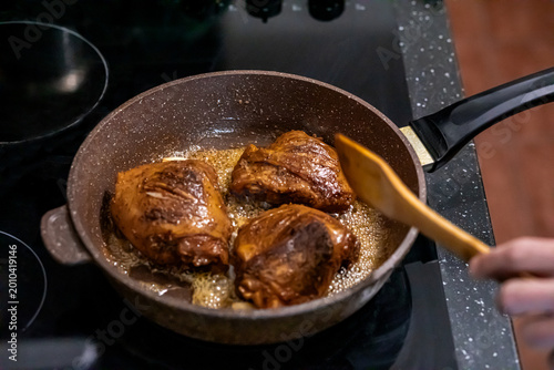 Foto Woman frying chicken thighs in nonstick pan on induction stove