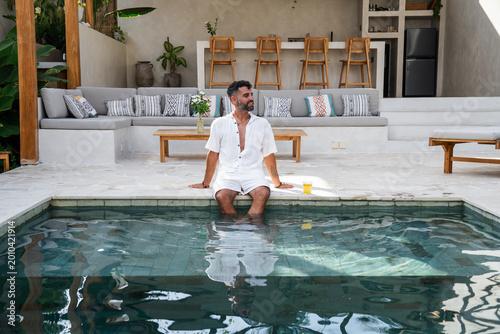 Young man enjoying summer vacation, feeling refreshed by a swimming pool at a modern villa