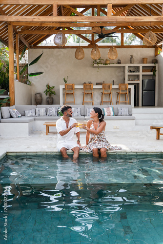Young couple enjoying drinks by a swimming pool in a tropical resort villa