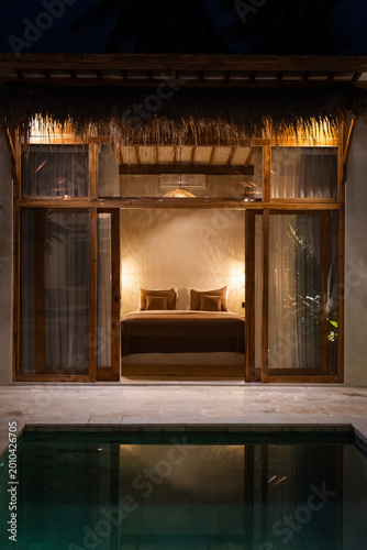 Cozy illuminated bedroom and swimming pool of a luxury modern tropical resort villa