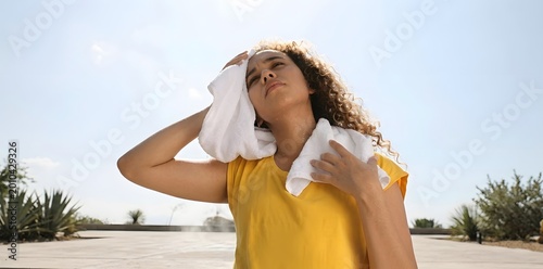 Tired woman wiping sweat with a towel outdoors in summer