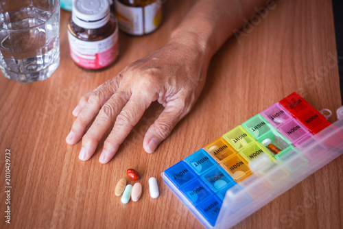 Senior woman's hand and variety of medical pills, preparing to take her daily dose from a pillbox. Concept of geriatric healthcare, managing multiple medications, and pharmaceutical treatment.