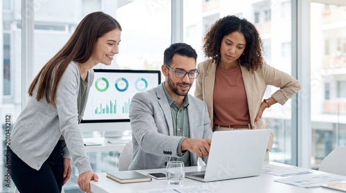 Businessman pointing at laptop screen while explaining project to female colleagues in office
