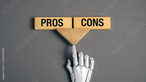 White robot finger pointing at a balance of pros and cons wooden blocks on a grey background illustrating artificial intelligence decision making.
