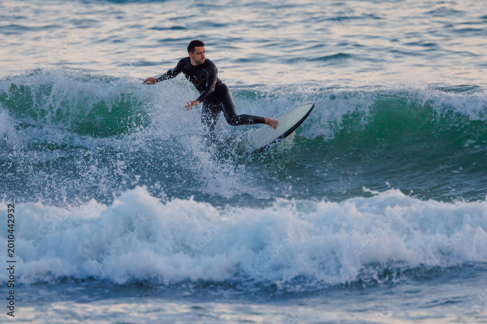 Obraz premium Surfer on surfboard riding ocean wave at evening light