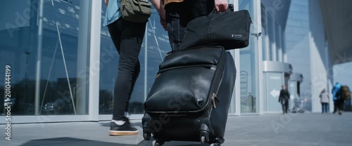 Unrecognizable couple holding hands and walking with a suitcase outside a modern airport terminal