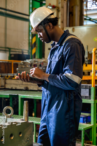 Canvas-taulu Black industrial engineer man using tablet working in heavy industry factory