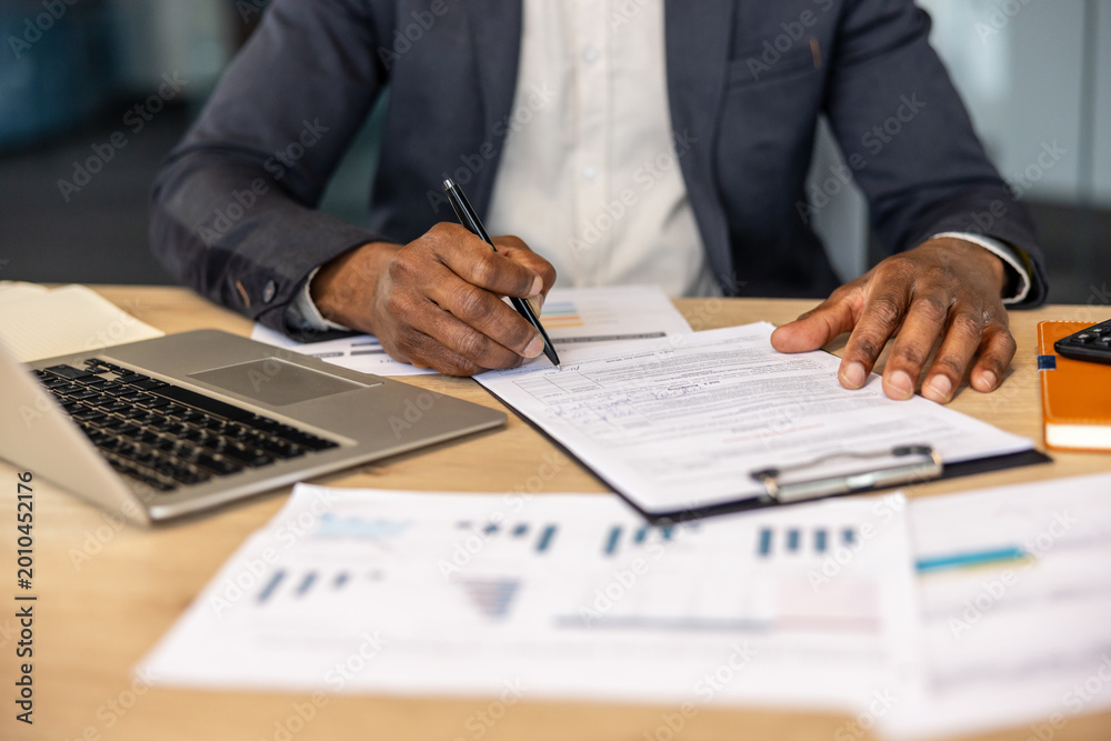 Fototapeta premium Entrepreneur signing a business contract, focusing on legal paperwork at a modern office desk with a laptop and financial documents, symbolizing agreement, success, and official procedures