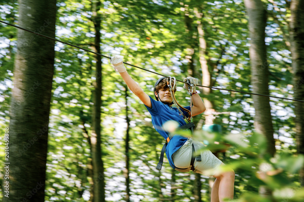 Obraz premium Teenage boy climbing rope course in forest adventure park, child wearing helmet and harness enjoying outdoor challenge, real life.