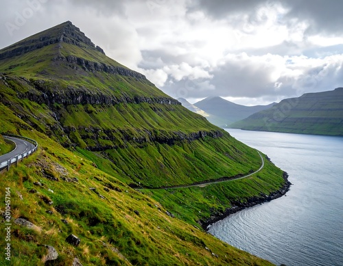 Winding road hugs green coastal mountains beside calm water under clouds
