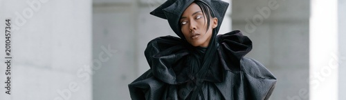 Model wearing sculptural black outfit posing in concrete setting