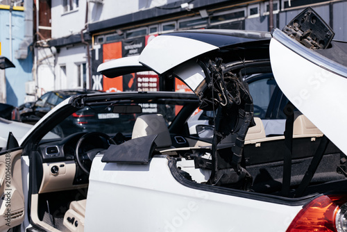 Repair process of a white convertible hardtop roof in a specialized car service. View of the open hydraulic mechanism and car interior during technical maintenance.