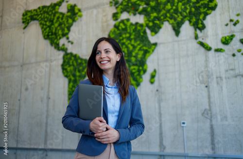 Businesswoman holding laptop smiling in front of green world map