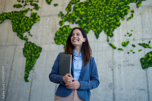 Businesswoman standing in front of world map looking at green map